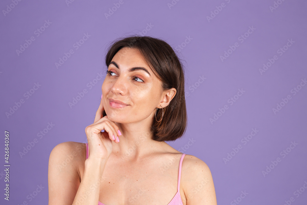 Young brunette in top isolated on purple background looks to the side thoughtfully with a sweet smile Young brunette in top isolated on purple background looks to the side thoughtfully with a sweet smile