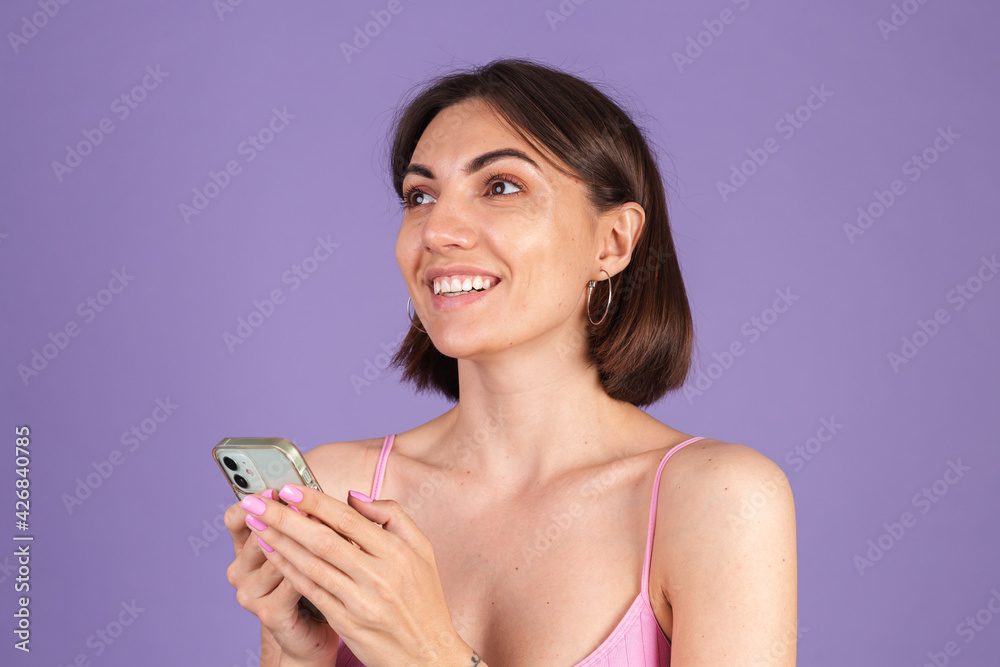 Young brunette in top isolated on purple background holding mobile phone with big smile happy excited face, chatting, having conversation Young brunette in top isolated on purple background holding mobile phone with big smile happy excited face, chatting, having conversation