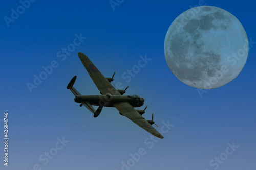 An Avro Lancaster World War II era heavy bomber flying in the light of a full moon