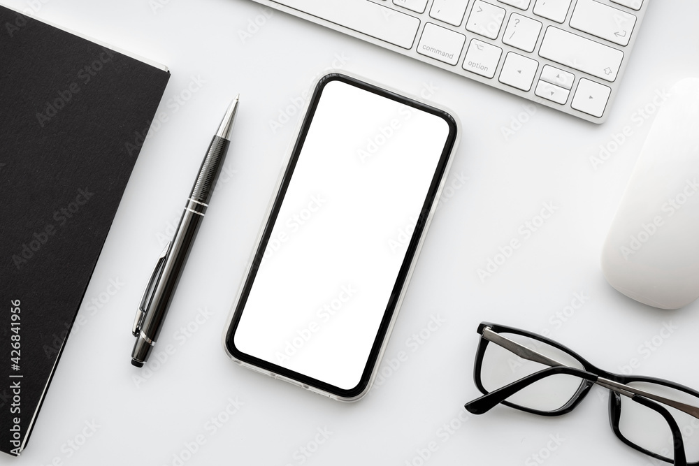 Smartphone with blank mockup screen is on top of white office desk table with supplies. Top view with copy space, flat lay. Smartphone with blank mockup screen is on top of white office desk table with supplies. Top view with copy space, flat lay.