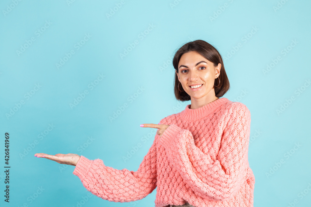 Young brunette in pink sweater isolated on blue background happy amazed excited point left with finger Young brunette in pink sweater isolated on blue background happy amazed excited point left with finger