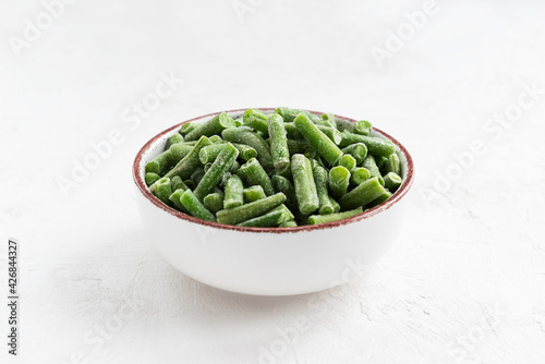 Frozen green beans in a bowl on a white table.