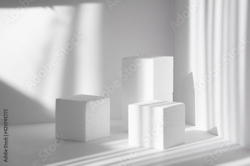 3d podium  for presentations of packaging and cosmetics. Three white styrofoam cubes  of different heights  against background of clean walls  shadow from the harsh sunlight like streaks