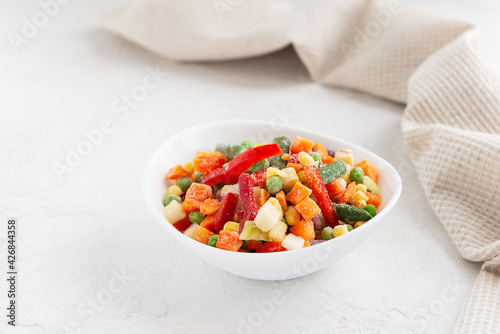 Mix of frozen vegetables in a bowl on a white table.