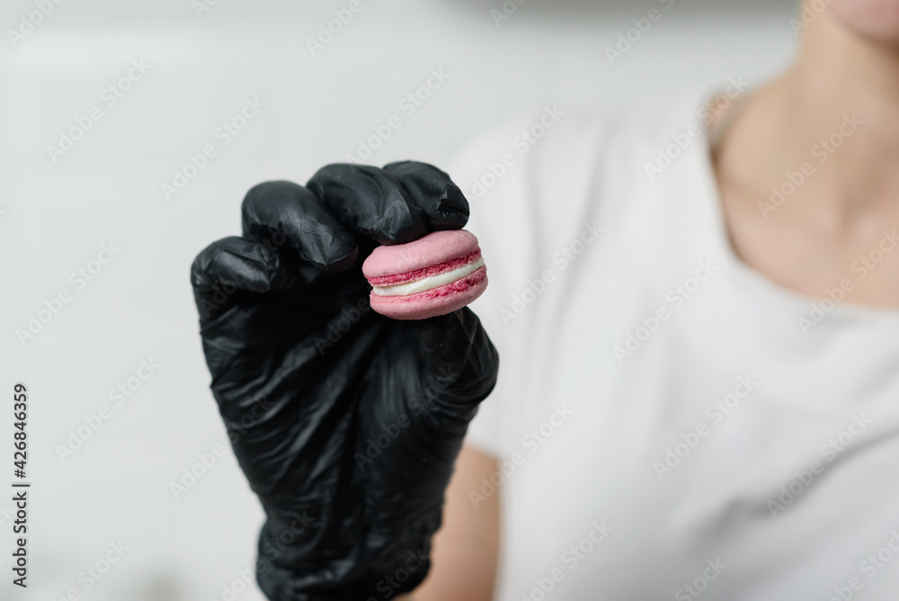 A gloved female hand holding a macaroni cookie or a macaroni dessert A gloved female hand holding a macaroni cookie or a macaroni dessert