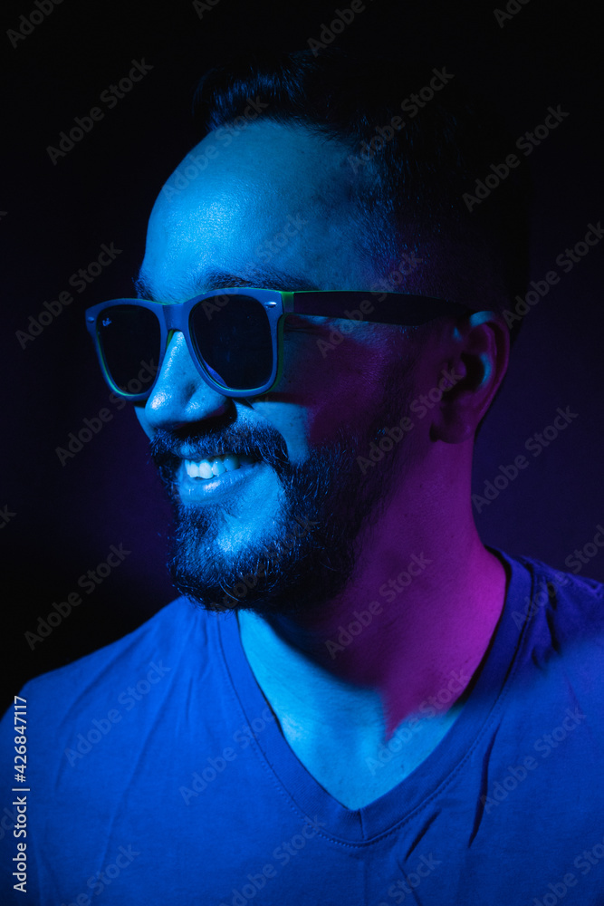 Retrato de hombre joven con barba y gafas de sol sonriendo con un fondo negro Retrato de hombre joven con barba y gafas de sol sonriendo con un fondo negro