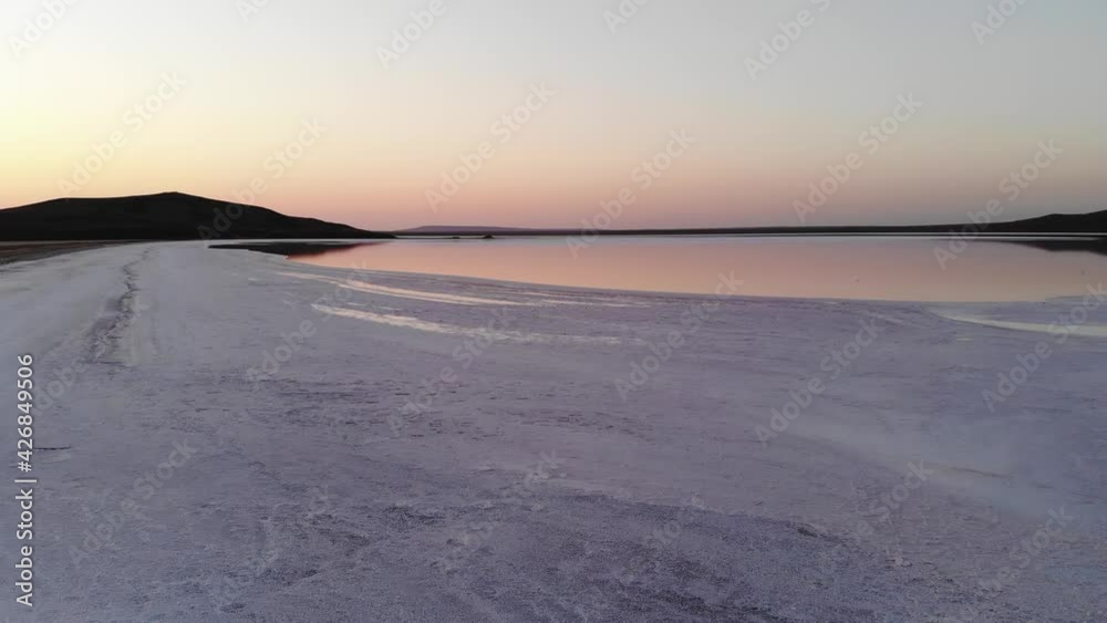 Aerial view of flying over the salty shore of pink salt lake in the evening at dusk, blue sky reflection in pink water