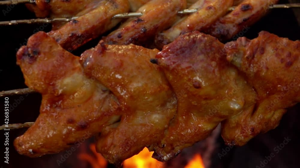 Close-up of delicious marinated chicken wings on the skewers rotated above the open fire outdoors Close-up of delicious marinated chicken wings on the skewers rotated above the open fire outdoors