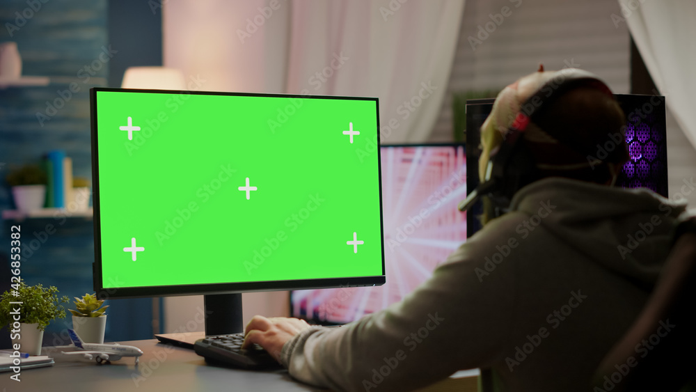 Professional cyber gamer playing video games with greenscreen, chroma key, mock up desktop isolated display. Player using powerful computer with mockup screen streaming shooter games wearing headset