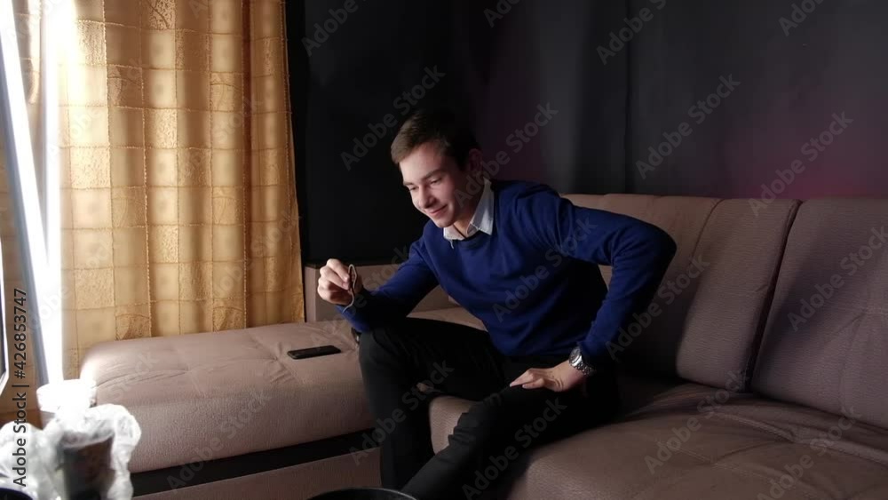 The guy sits on the couch and holds a live worm in his hand. Before eating a worm, he thinks and smiles. Portrait of young caucasian man sincere emotions. Nasty unpleasant food.