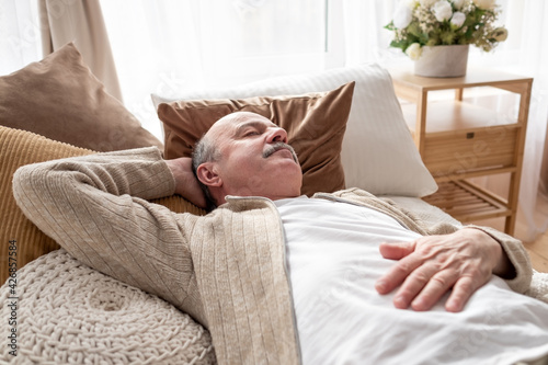 Senior man asleep in bed at home napping after breakfast