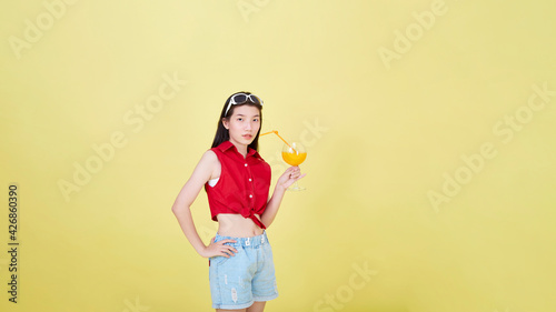 Woman drinking juice in summer on yellow background