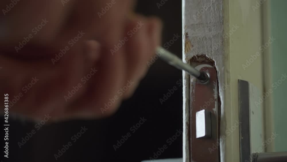 Male hand holds screwdriver and turns metal screw in door lock. Male hand holds screwdriver and turns metal screw in door lock.
