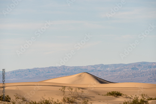 Sand dunes in the desert with hazy mountain beyond under light hazy sky.