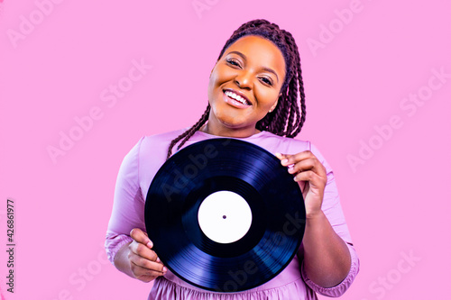 hipster lady with cool dreadlocks pigtails showing old fashion school vinyl in pink studio background