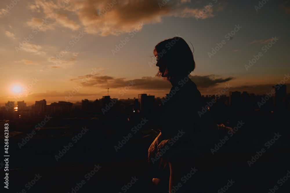 Girl on the roof of a building against the backdrop of a sunset in the city