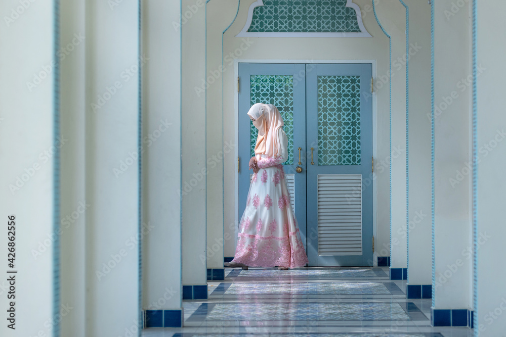 Fototapeta premium Beautiful Muslim woman in traditional clothing walks in the aisle of the mosque, covering her face with a scarf