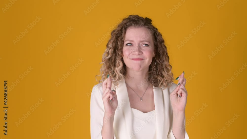 Young attractive girl with curly hair makes a wish with her fingers crossed on a yellow studio background. People lifestyle concept Young attractive girl with curly hair makes a wish with her fingers crossed on a yellow studio background. People lifestyle concept