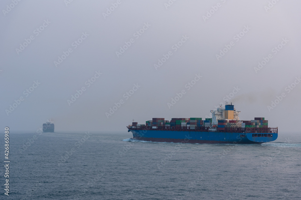 Cargo container ship departing from port of Xiamen. She is beginning voyage on her international trade route. Foggy morning and sunrise near Chinese coast.
