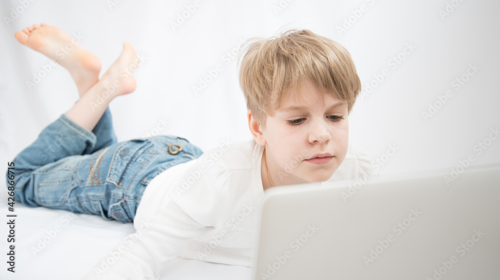 The blond child looks attentively at the computer or laptop screen. Close-up portrait The blond child looks attentively at the computer or laptop screen. Close-up portrait