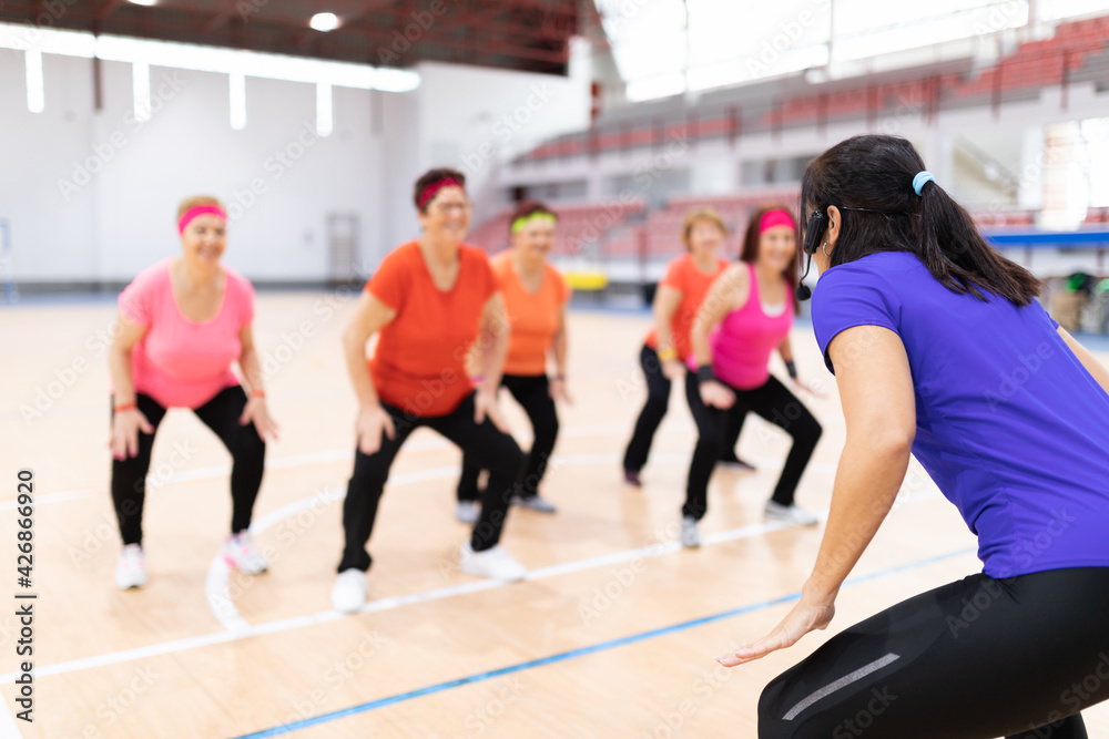 Obraz premium young girl sports monitor in sports center giving collective classes to older women for maintenance
