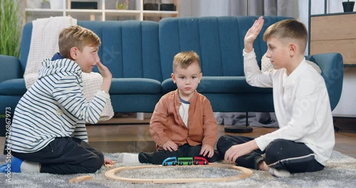 Likable happy satisfied different ages brothers had gathered car track on the floor at home and giving high five each other before starting to play photo