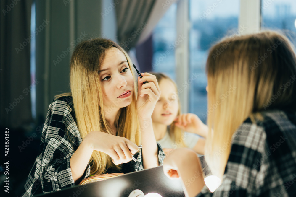 Stylish girl in a plaid shirt with cosmetics puts mascara on the eyelashes. Teen in the dressing room in front of the mirror makes a make-up. person before the party. Taking self-care. Beauty concept