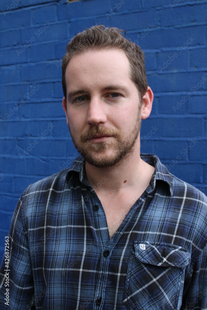 attractive male in blue plaid shirt against blue background painted wall relaxed and confident attractive male in blue plaid shirt against blue background painted wall relaxed and confident