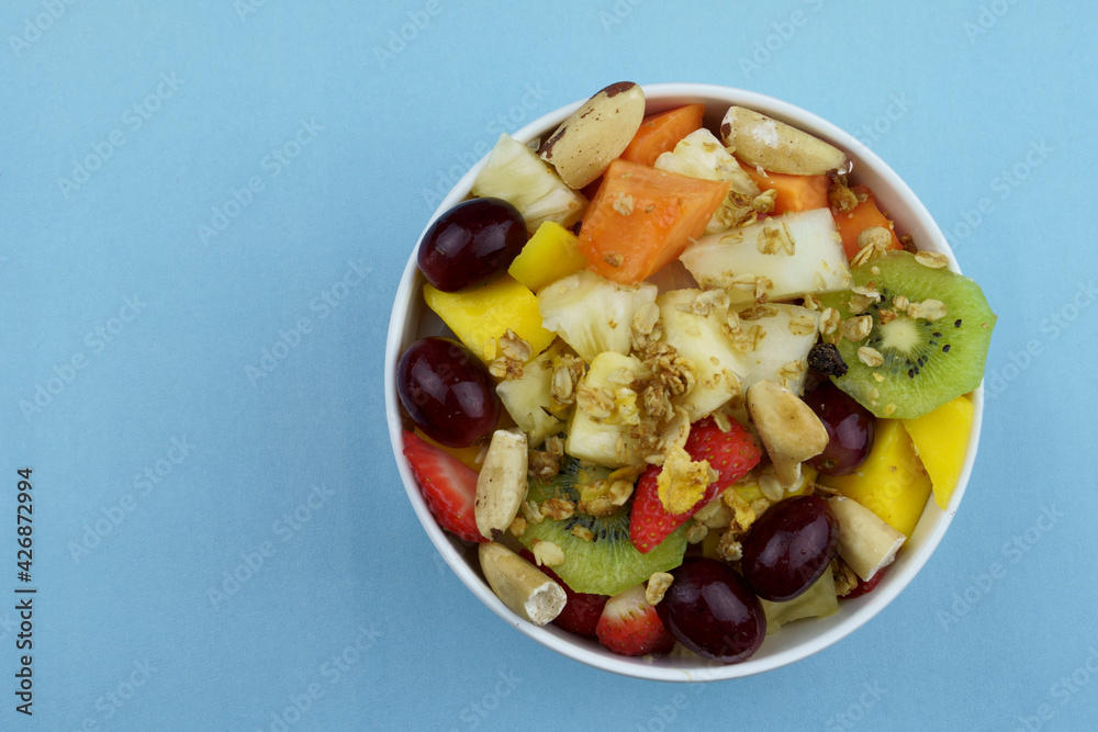 Fruit salad with chestnuts and granola in a bowl. Multicolored ripe fruits. Pineapple, mango, grape, strawberry, papaya, melon, banana and kiwi. Top view. Fruit salad with chestnuts and granola in a bowl. Multicolored ripe fruits. Pineapple, mango, grape, strawberry, papaya, melon, banana and kiwi. Top view.