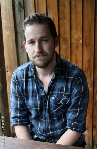 attractive male in blue plaid shirt against wooden fence background relaxed and confident portrait 
