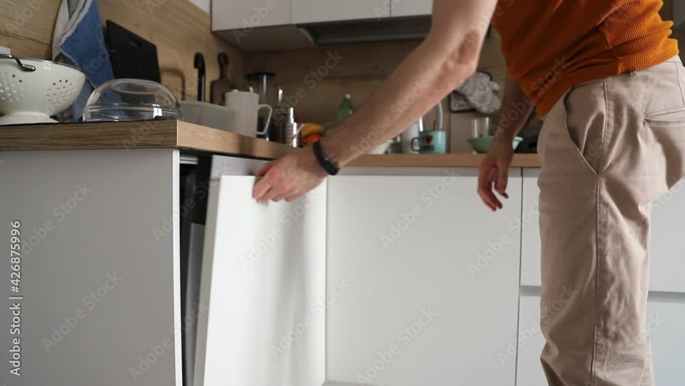 A man opening and closing the dishwasher. Washing dishes in the dishwasher. The man doing chores A man opening and closing the dishwasher. Washing dishes in the dishwasher. The man doing chores