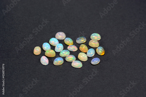 Natyral Ethiopian opal small cabochons lot on black background. White opaque stone base with multicolor flashes. Unheated untreated earth mined gemstones. photo