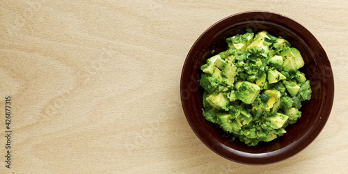 Bowl of freshly made chunky guacamole on wooden table with copy space for text, top view.