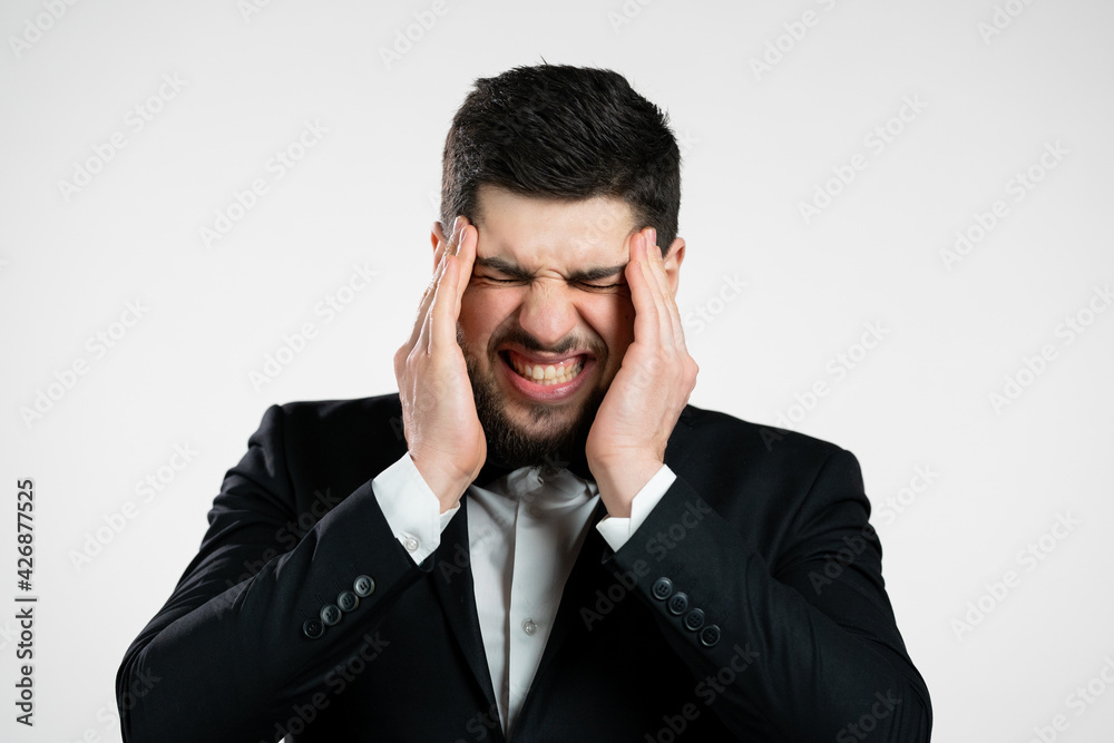 Young man having headache, studio portrait. Guy in tuxedo putting hands on head, isolated on white background. Concept of problems, medicine, illness Young man having headache, studio portrait. Guy in tuxedo putting hands on head, isolated on white background. Concept of problems, medicine, illness