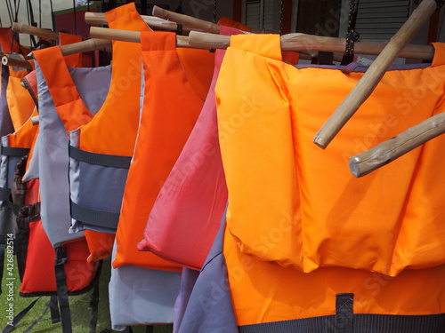 Colorful water life vest. Life jackets hanging on clothes line. Buoyancy jackets on a rail. Water sports safety accessory. Sports equipment pattern.
