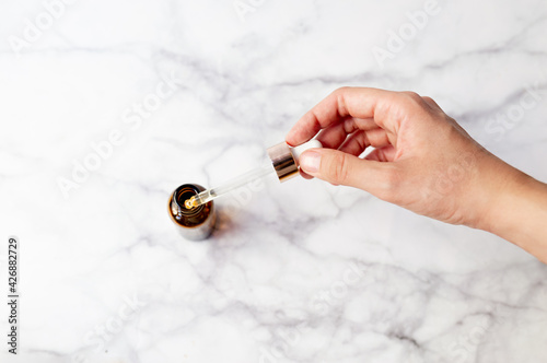 Top view of hand holding a retinol oil serum pipette and oil bottle on isolated marble background. Beauty care concept. photo