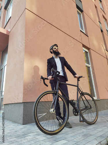 A young stylish businessman pushing a bicycle while going to work.