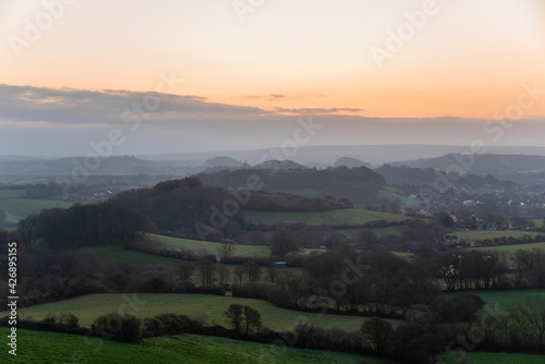 Beautiful vibrant sunrise landscape image of misty view towards Symondsbury village in Dorset on a Spring morning