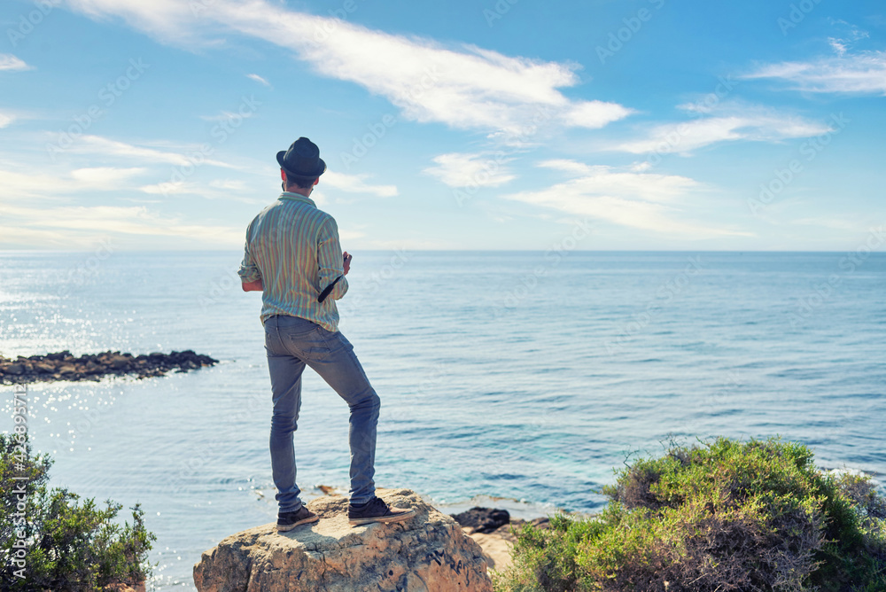 A man traveler observes the ocean from a hill