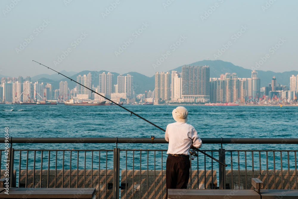 fisher man with fishing rod and city skyline background in Hong Kong fisher man with fishing rod and city skyline background in Hong Kong