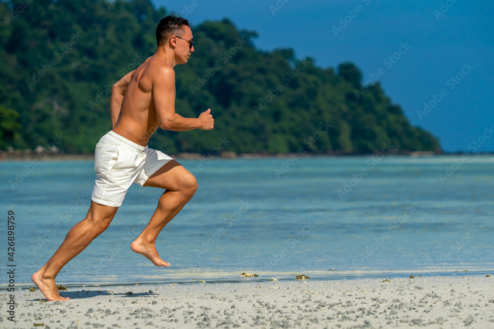 Young Man In Fitness Clothing Running Along Beach outdoors