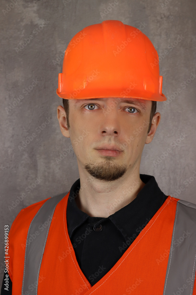 Construction worker in a yellow vest with a helmet in hand on gray background. Vertical orientation Construction worker in a yellow vest with a helmet in hand on gray background. Vertical orientation