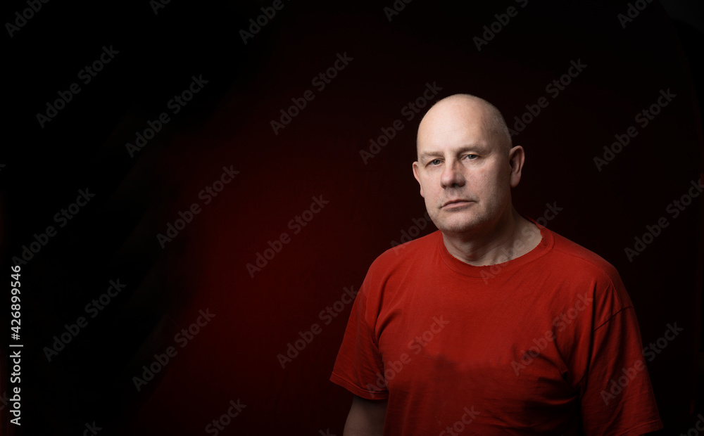 Studio portrait of middle-aged man serious face looking at camera isolated on dark red light background Studio portrait of middle-aged man serious face looking at camera isolated on dark red light background