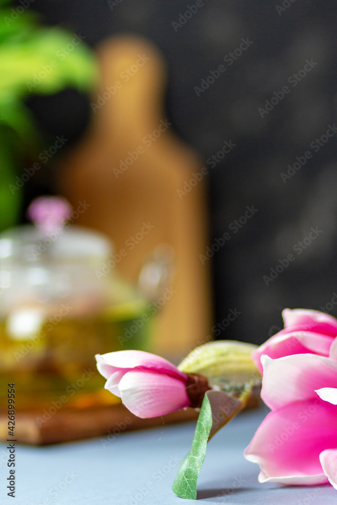 green tea with rose petals in a transparent teapot on a wooden table on a black background. The background is blurred. Tea drinking.