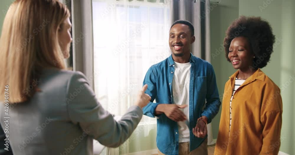 Close up of pretty happy Caucasian woman real estate realtor giving keys to new apartment to young African American couple. Cheerful clients receiving keys buying home. Tenant agreement House purchase Close up of pretty happy Caucasian woman real estate realtor giving keys to new apartment to young African American couple. Cheerful clients receiving keys buying home. Tenant agreement House purchase