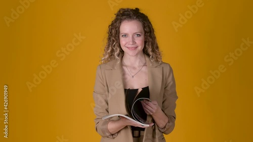 A young attractive girl with curly hair leafs through a glossy magazine on a studio yellow background. searching for ideas