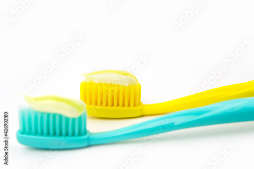 Blue and yellow toothbrushes with yellow striped paste on white isolated background.