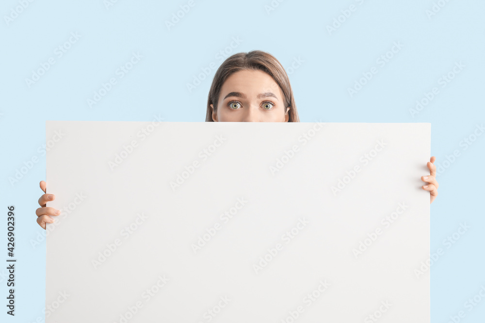Surprised young woman with blank poster on color background Surprised young woman with blank poster on color background