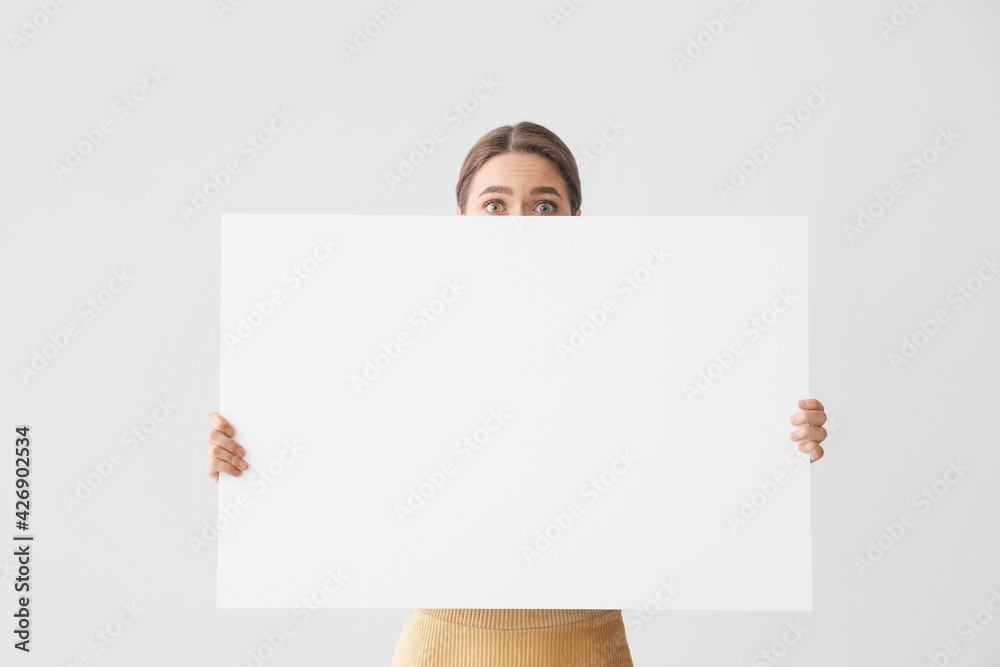 Surprised young woman with blank poster on light background Surprised young woman with blank poster on light background