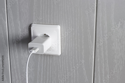 Charger power supply is connected to electrical outlet on wall photo